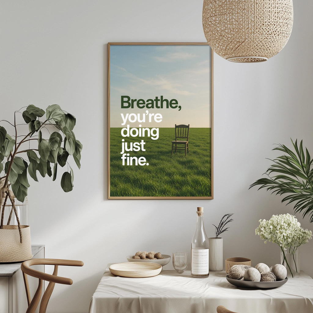 a dining table with a bowl of fruit, a bottle, and a vase of flowers, along with a framed poster on the wall that reads "Breathe, you're doing just fine."