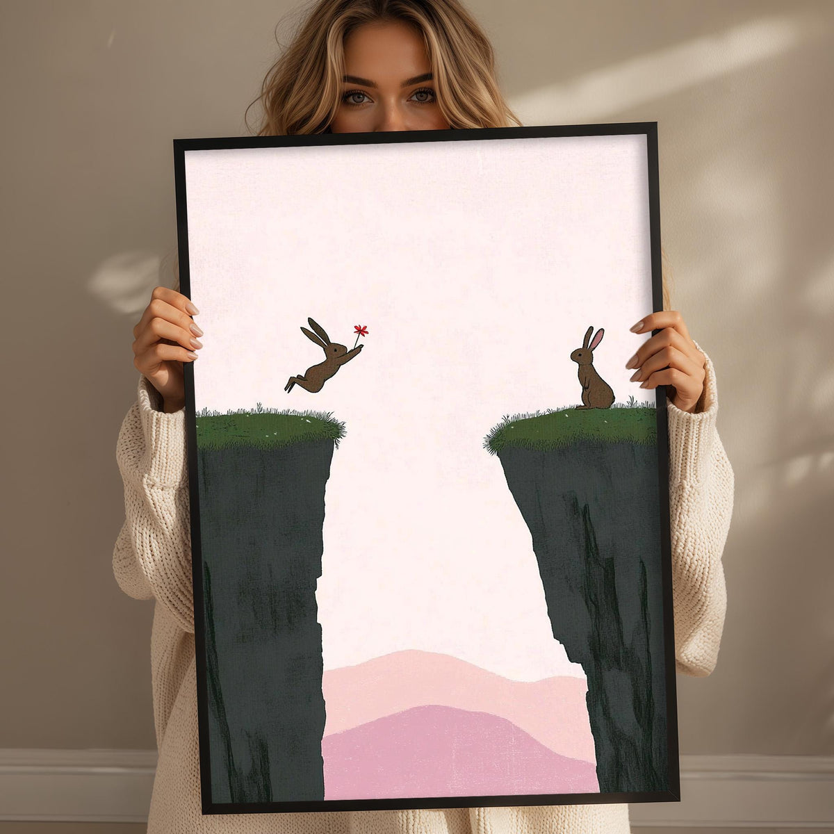 A woman holds up a framed print depicting two rabbits on a cliff, with one rabbit jumping over the other.