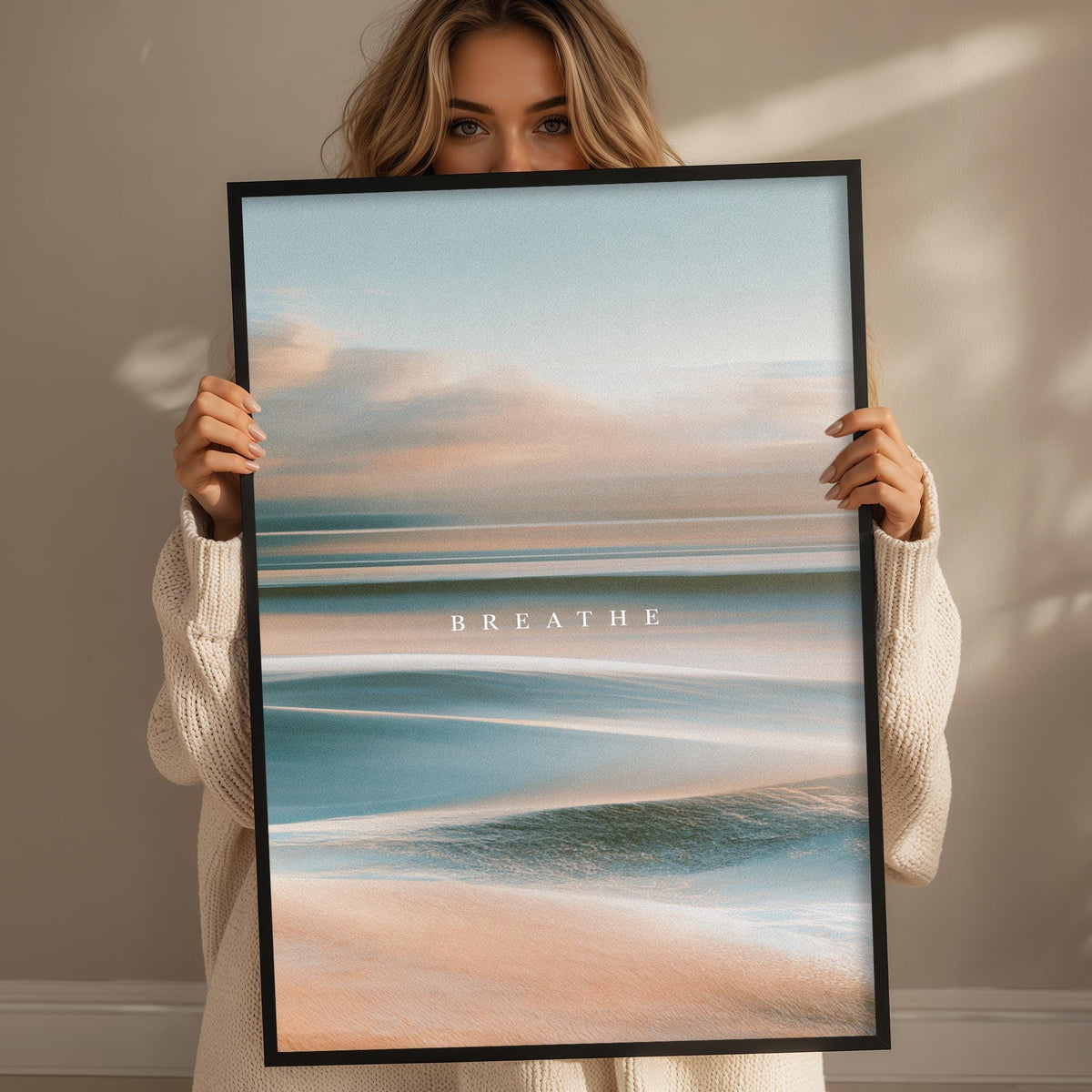 A woman holding a framed picture of a beach with the word "BREATHE" written on it.