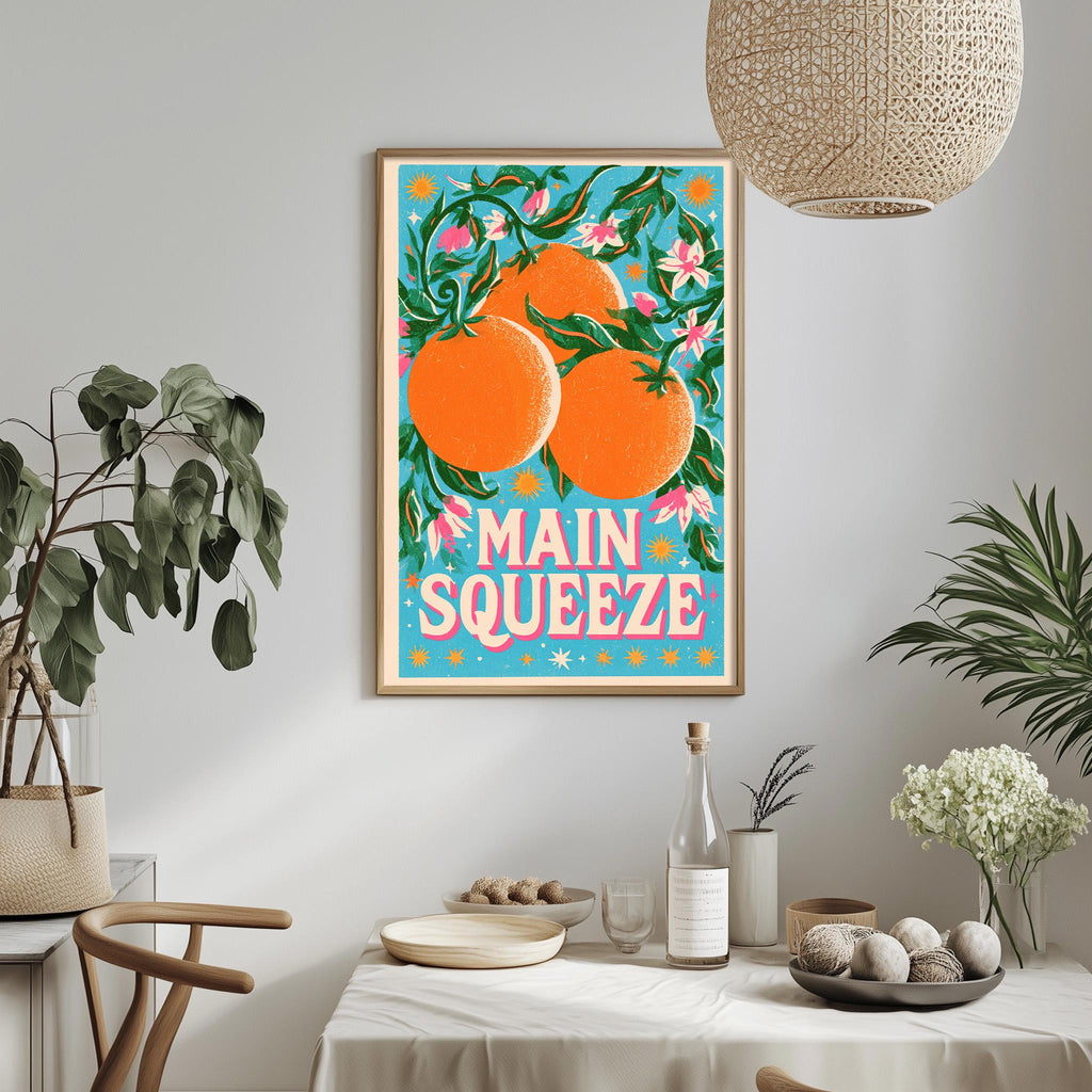 a framed poster of oranges hanging on a wall, with a dining table and chairs in the foreground.