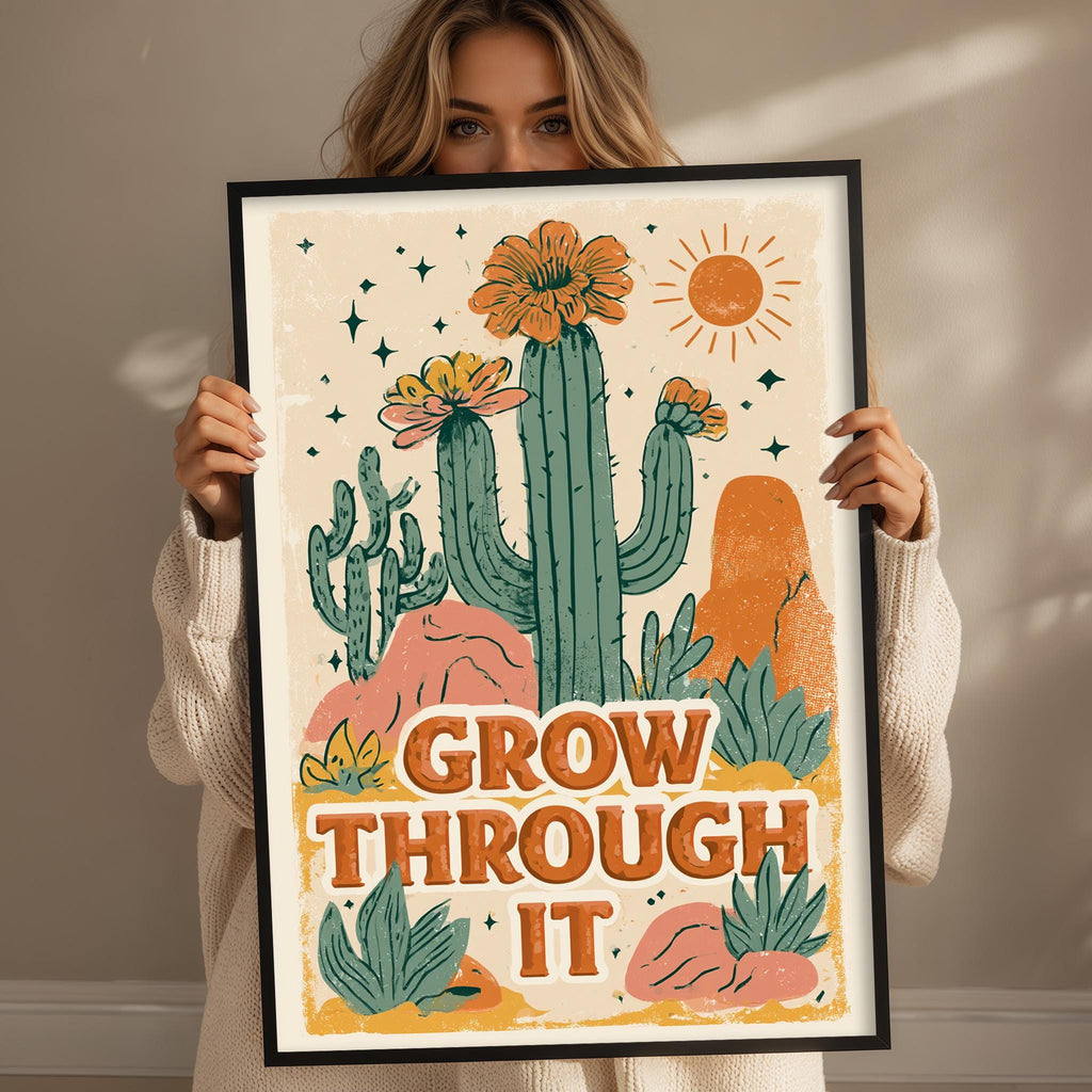 A woman holding a framed poster with a desert-themed illustration and the text "GROW THROUGH IT".