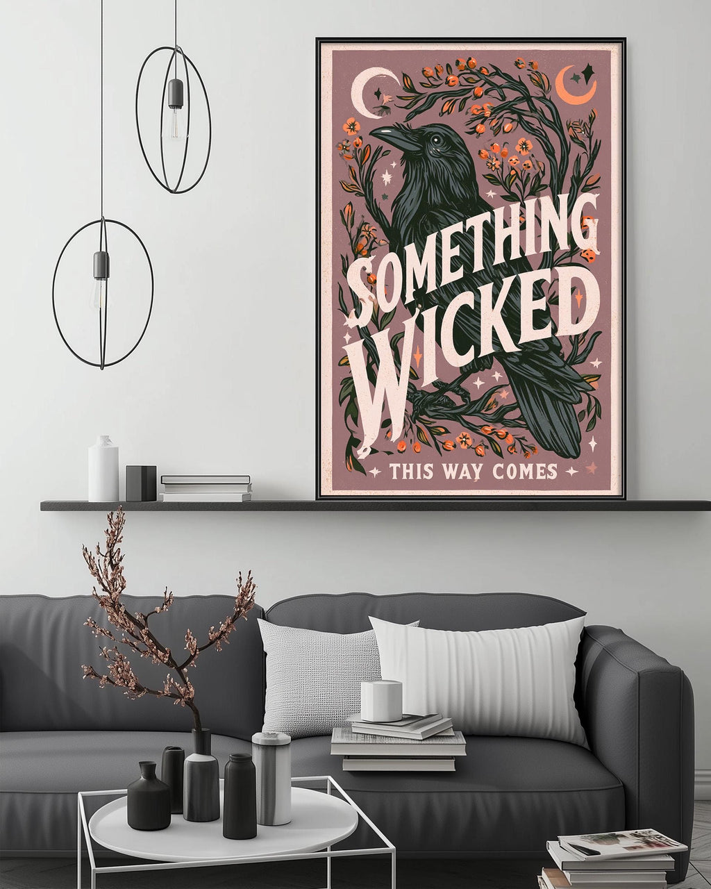 a living room with a gray couch, a coffee table, and a framed poster on the wall. The poster has a whimsical design with a bird and a crescent moon, and the text "Something Wicked This Way Comes" is prominently displayed.