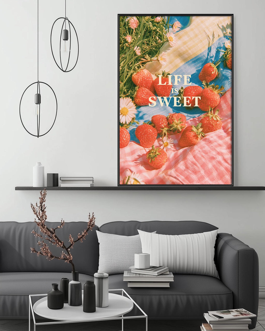 a cozy living room with a gray sofa, a coffee table, and a large framed poster of strawberries on the wall. The poster has the text "Life is sweet" written on it.