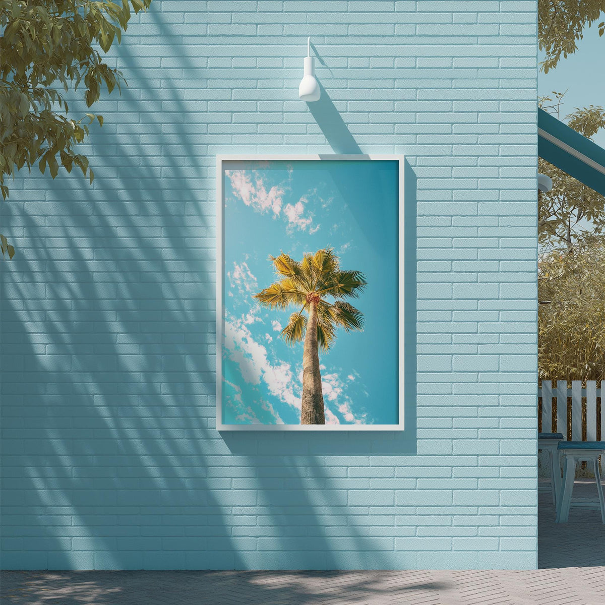 A framed photograph of a palm tree is displayed on a light blue brick wall, with a white light fixture hanging above it.