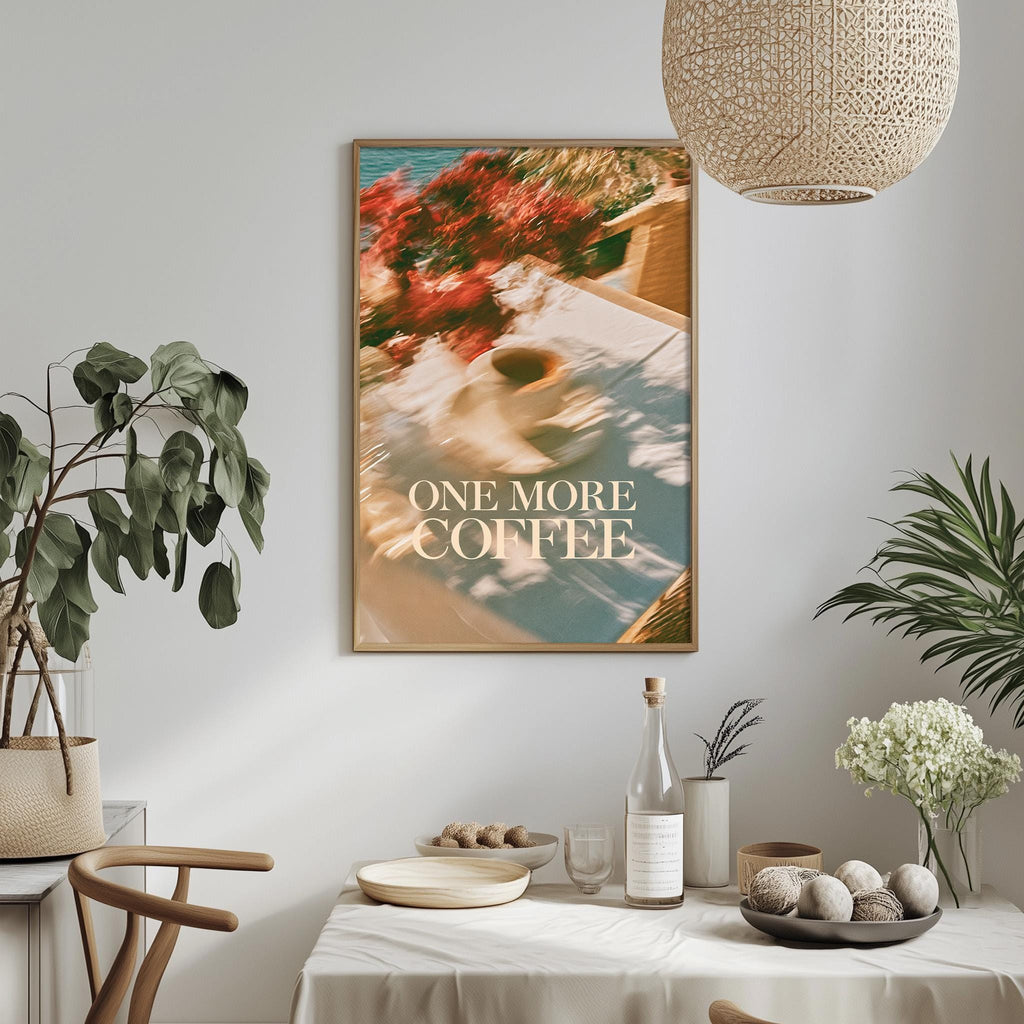 a dining table with a bowl of fruit, a bottle, and a vase, along with a potted plant and a hanging light fixture. Above the table, there is a framed poster with the text "ONE MORE COFFEE" displayed on it.