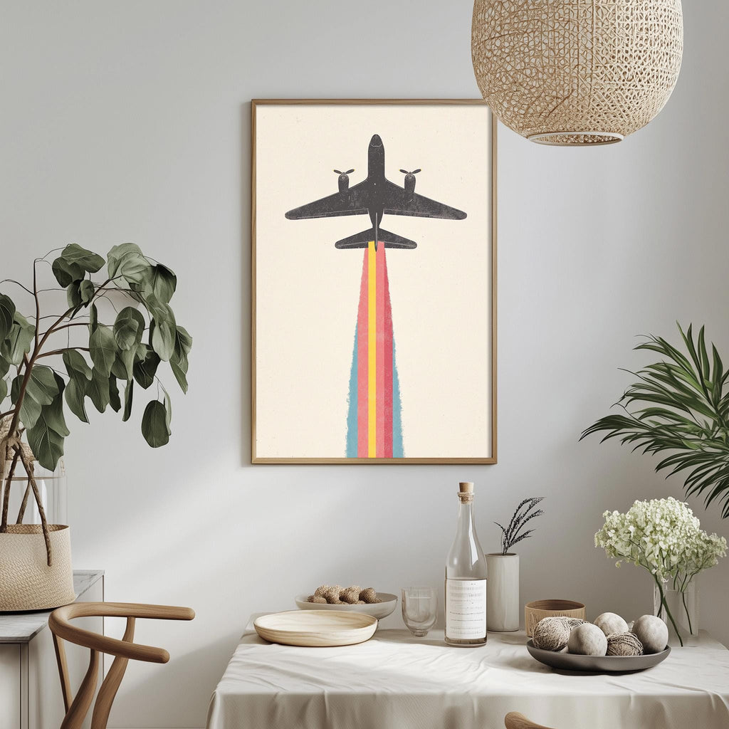 a dining table with a white tablecloth, a bowl of fruit, a bottle, and a vase with flowers. Above the table, there is a framed picture of a plane with a rainbow-colored smoke trail.