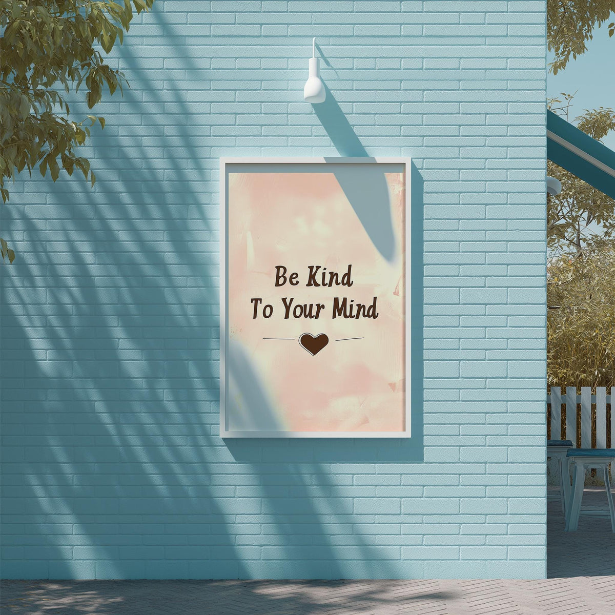 A framed poster with the text "Be Kind To Your Mind" is displayed on a blue brick wall, with a tree and a white light fixture above it.