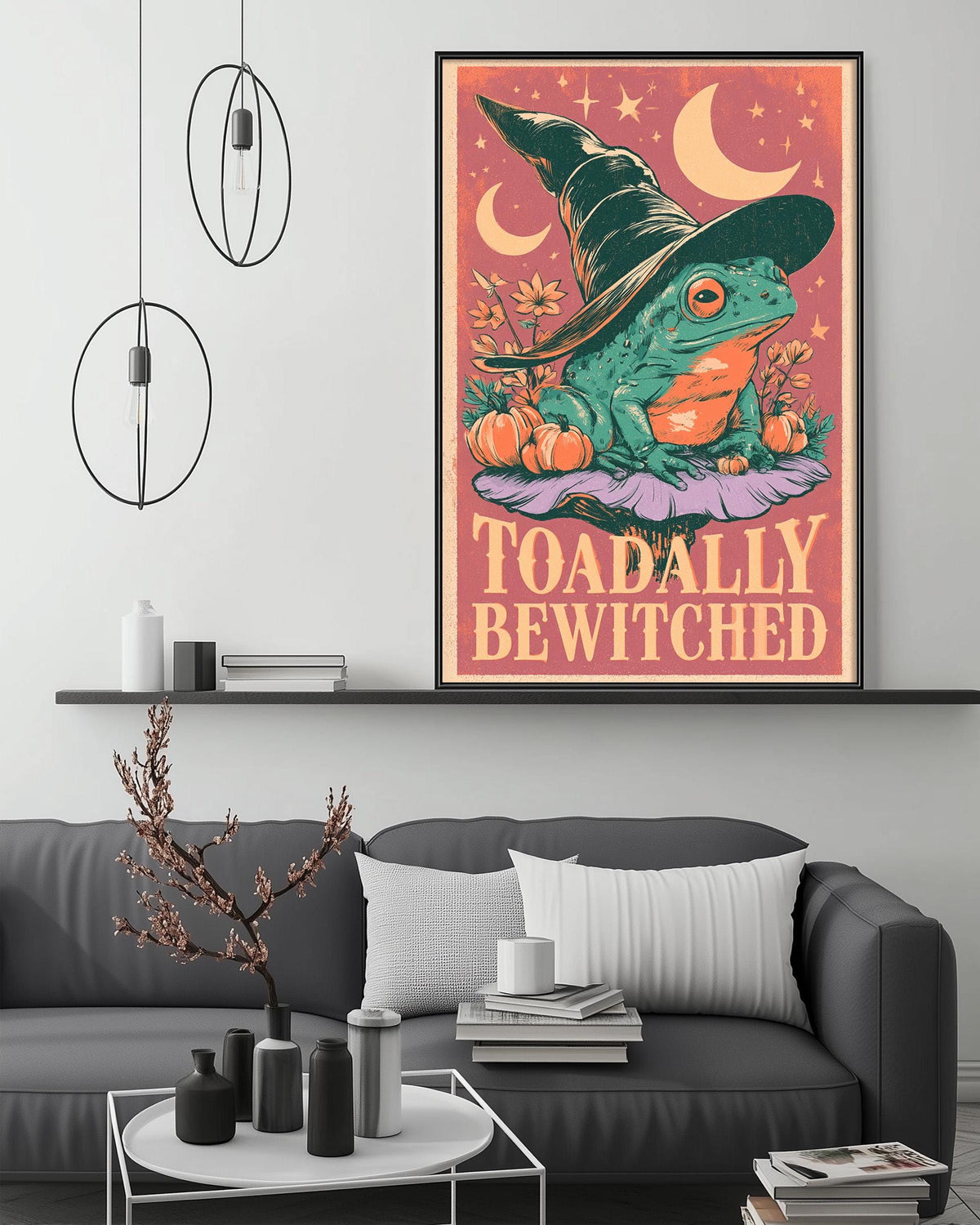 a poster of a frog wearing a witch's hat, surrounded by Halloween-themed elements such as pumpkins and crescent moons. The poster is displayed on a wall above a gray couch, which has a coffee table and decorative items on it.