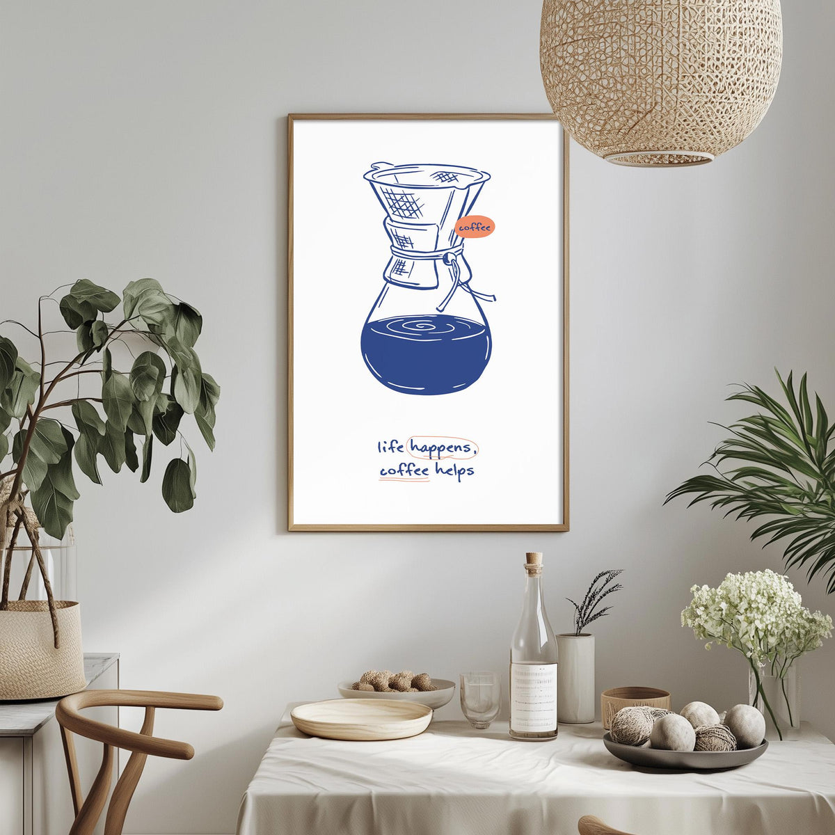 a framed illustration of a coffee maker on a wall, with the text "life happens, coffee helps" below it. The room has a dining table with a vase of flowers, a bottle, and a bowl of balls, creating a cozy and inviting atmosphere.