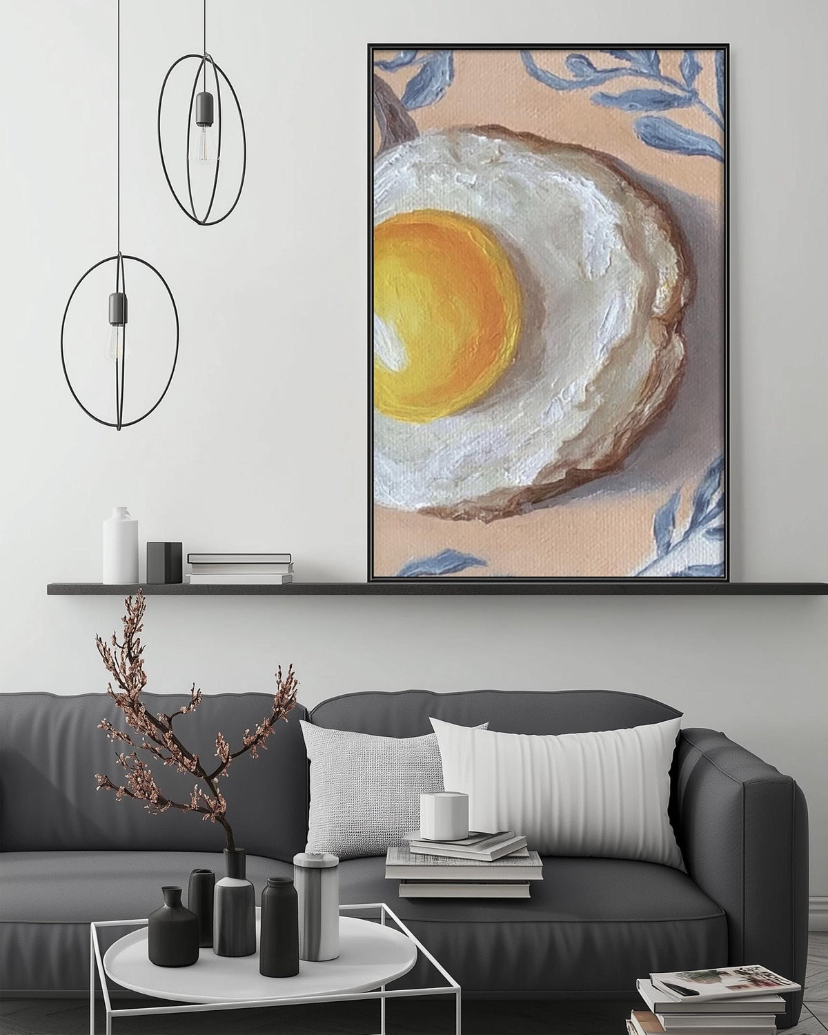a modern living room with a gray sofa, a coffee table, and a large painting of an egg on the wall. The painting is a vibrant mix of yellow and orange hues, with a white interior that contrasts with the warm tones. The room is decorated with various items, including a potted plant, a vase, and a stack of books, creating a cozy and inviting atmosphere.