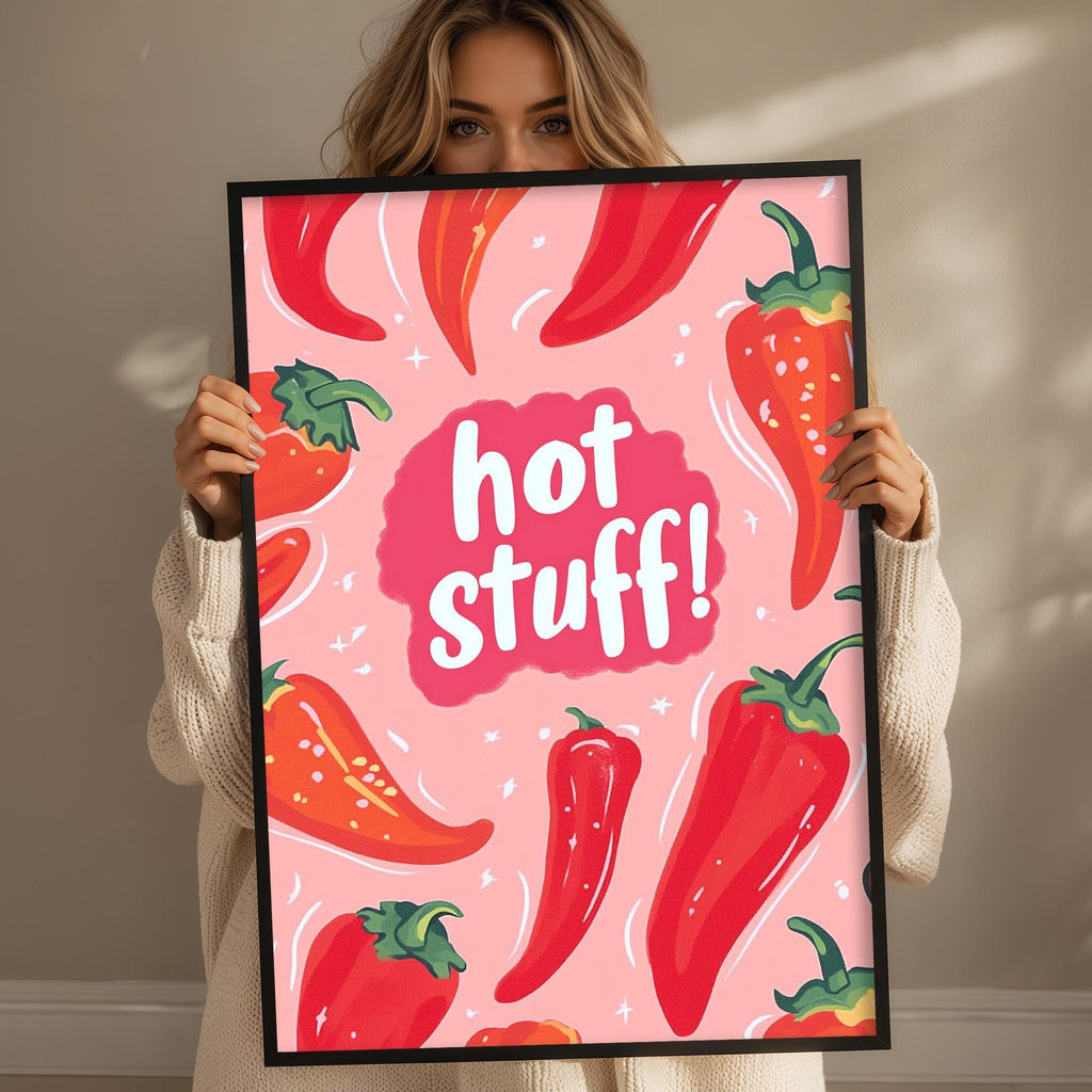 A woman is holding up a framed poster with a pink background and various red chili peppers.
