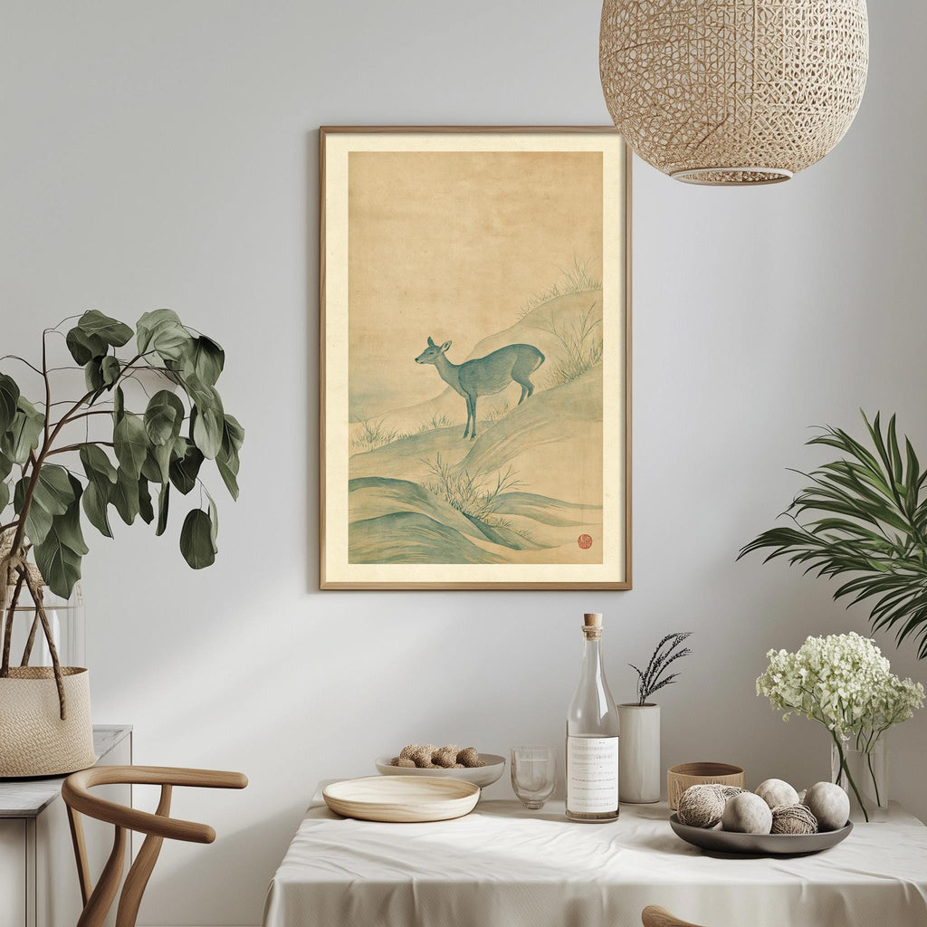 a dining table with a white tablecloth, a bowl of fruit, a bottle, and a vase with flowers. Above the table, there is a framed picture of a deer. The table is set with a potted plant, a hanging light fixture, and a plant in a vase.