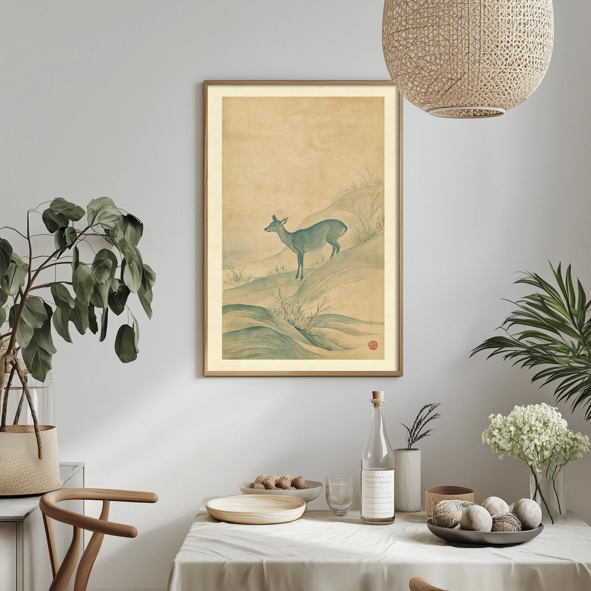 a dining table with a white tablecloth, a bowl of fruit, a bottle, and a vase with flowers. Above the table, there is a framed picture of a deer. The table is set with a potted plant, a hanging light fixture, and a plant in a vase.