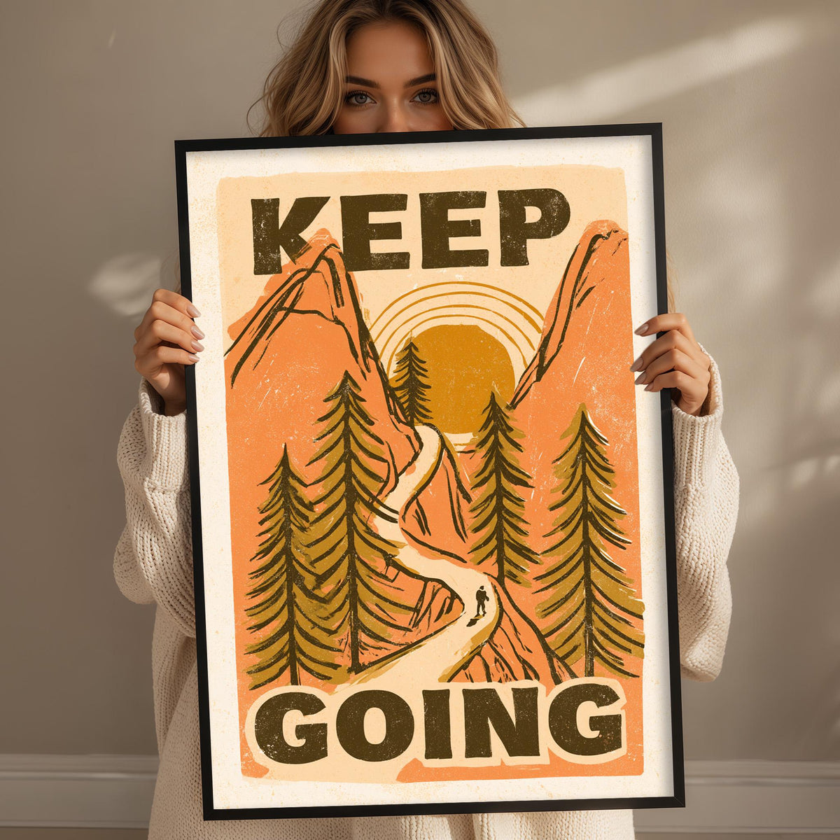 A woman holding a framed poster with a mountain landscape and the text "KEEP GOING" on it.