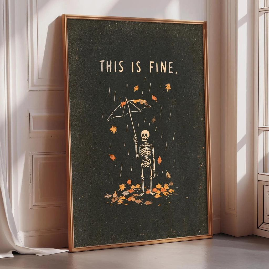 a framed poster with a skeleton holding an umbrella and surrounded by falling leaves, with the text "THIS IS FINE."