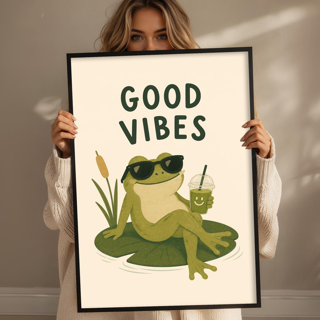A woman is holding up a framed poster with a cartoon frog sitting on a lily pad and drinking from a cup.