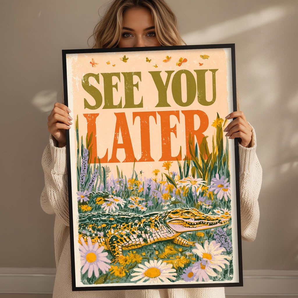 A woman is holding up a framed poster with a colorful illustration of a crocodile and flowers.