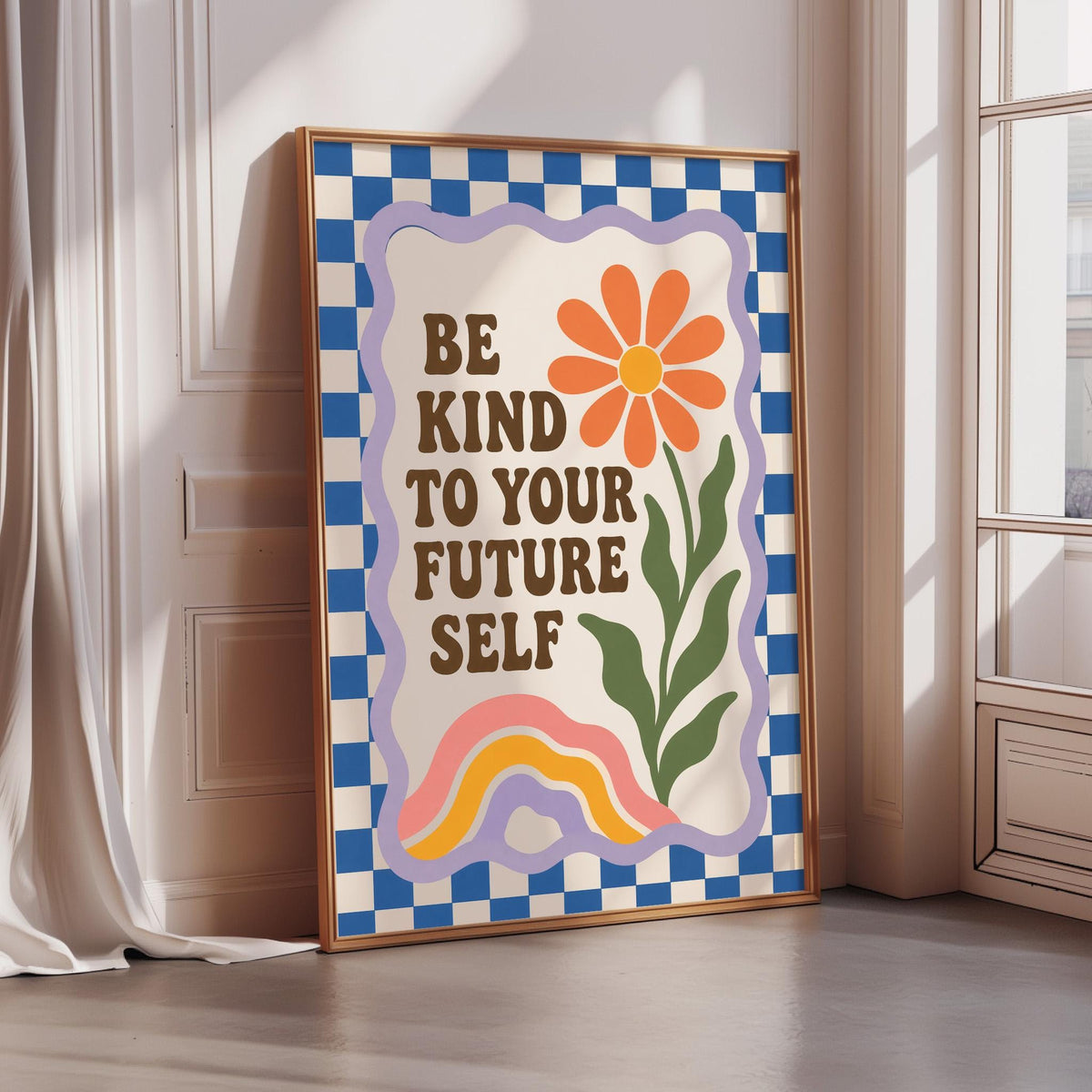 A framed poster with a flower and the text "Be kind to your future self" is displayed in a room with a window.