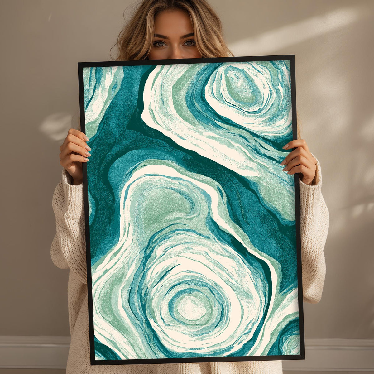 A woman is holding up a framed print with a striking abstract design featuring swirling patterns in shades of blue and green.