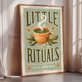 A framed poster with the text "LITTLE RITUALS MAKE GOOD DAYS" and an illustration of a cup of tea with steam rising from it.
