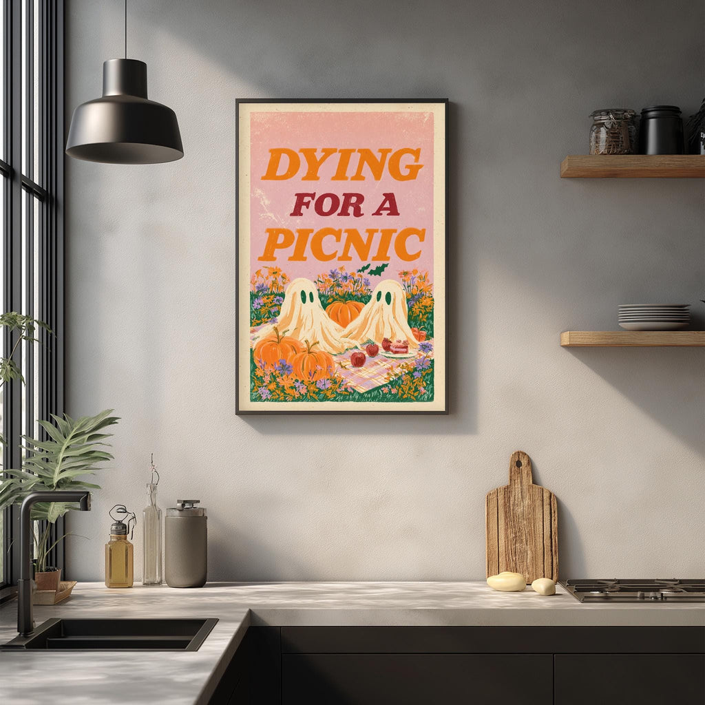 a kitchen counter with various kitchen items, such as a cutting board, a bottle, and a bowl. Above the counter, there is a framed poster with the text " Dying for a Picnic" and an illustration of two ghostly figures.