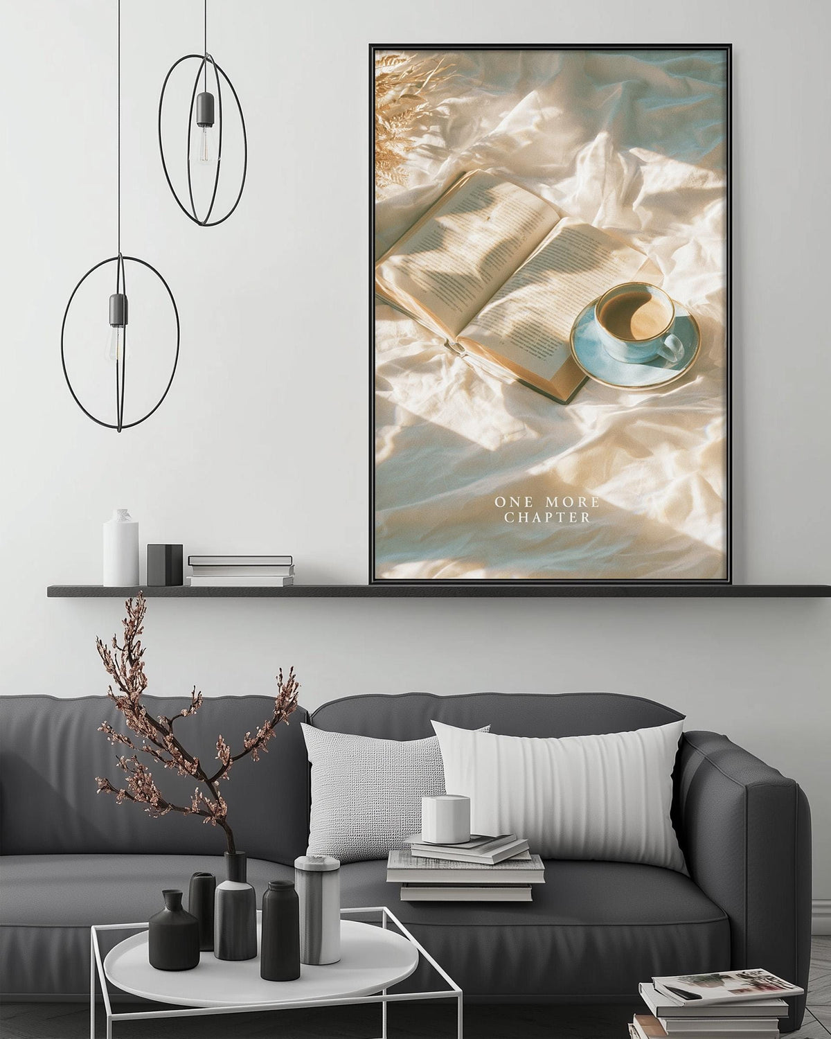 a cozy living room setting with a gray sofa, a coffee table, and a large framed poster of an open book with a cup of coffee on it. The poster is hanging on the wall above the sofa, and the room has a minimalist and modern design with pendant lights and a shelf displaying decorative items.