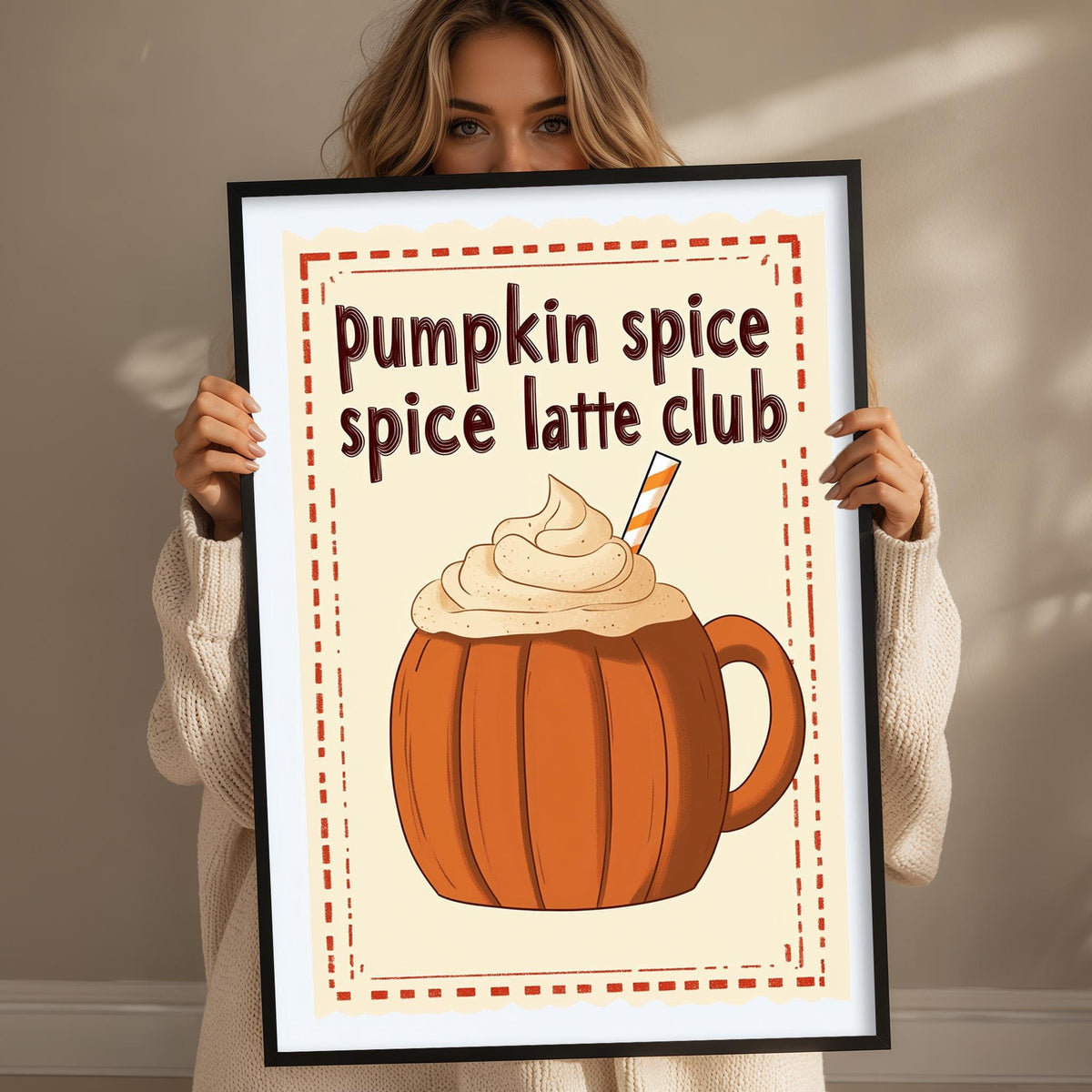 A woman holding a framed poster with an illustration of a pumpkin spice latte.