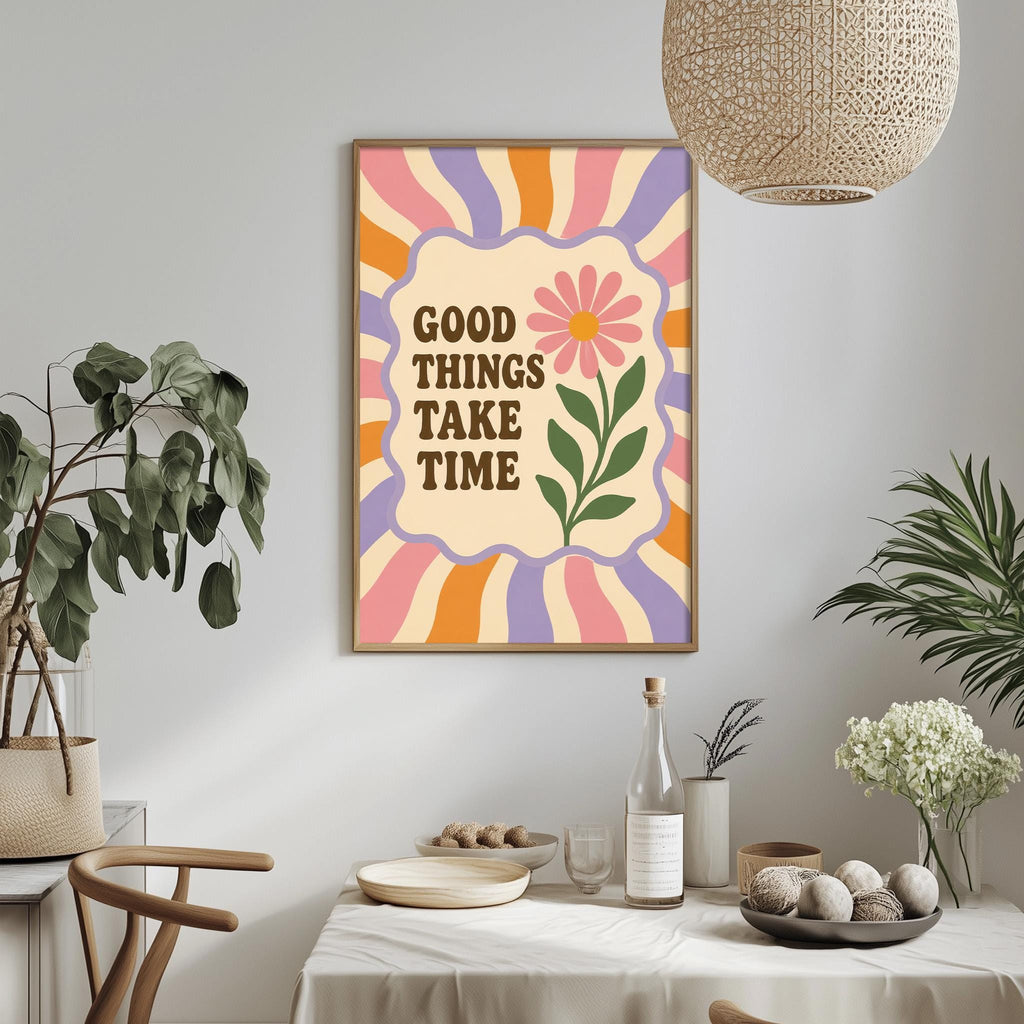 a framed poster with the text "GOOD THINGS TAKE TIME" on it, hanging on a wall above a dining table with various items on it, such as a bottle, a bowl, and a vase.