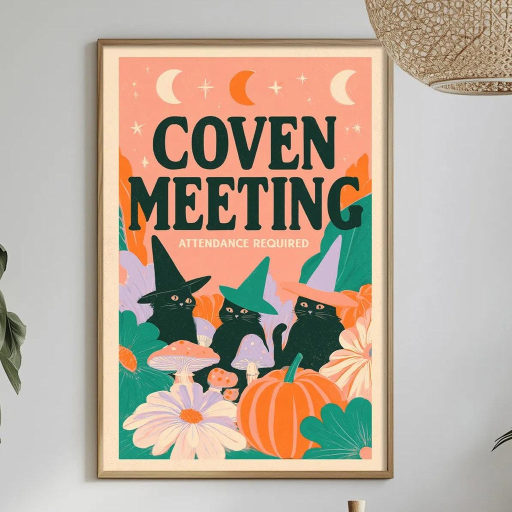 a framed poster with a whimsical illustration of cats and Halloween-themed elements, such as pumpkins and flowers, hanging on a wall above a dining table with various items on it.