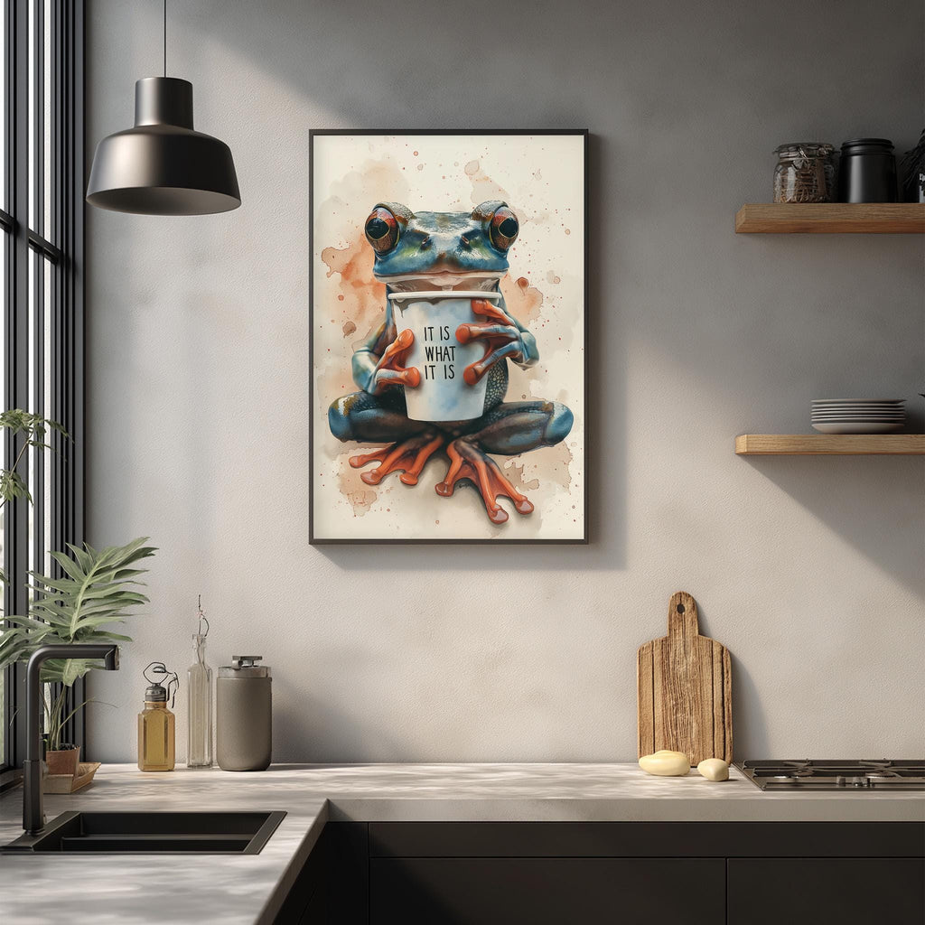 a framed painting of a frog sitting on a counter, holding a cup with the text "IT IS WHAT IT IS" written on it.