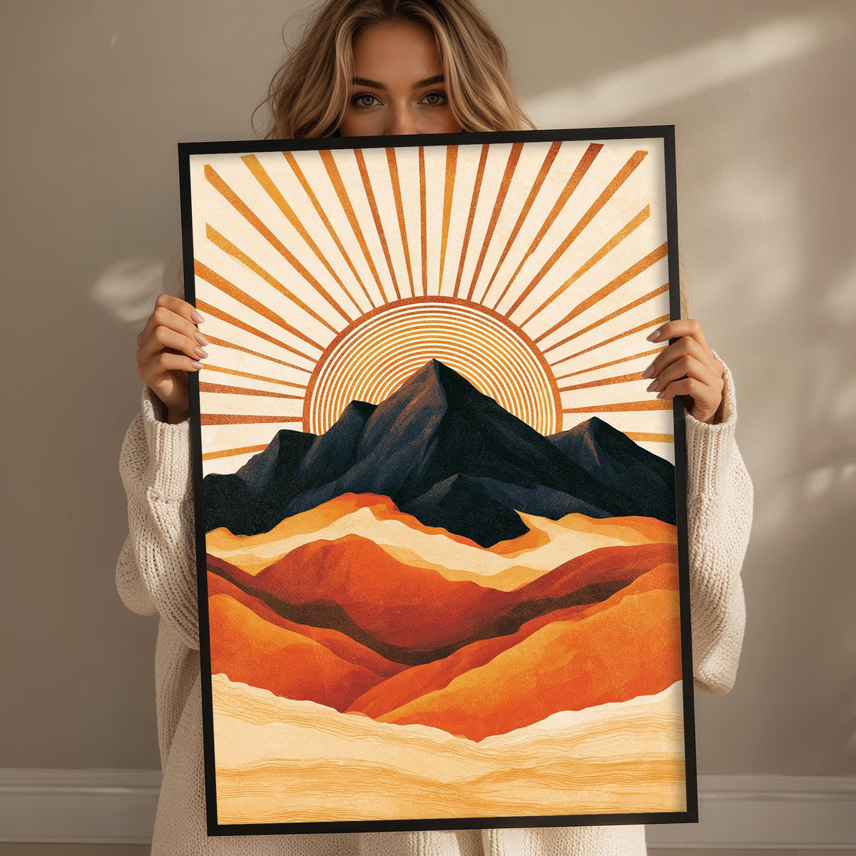 A woman holds up a framed print of a vibrant mountain landscape with a sunburst design.