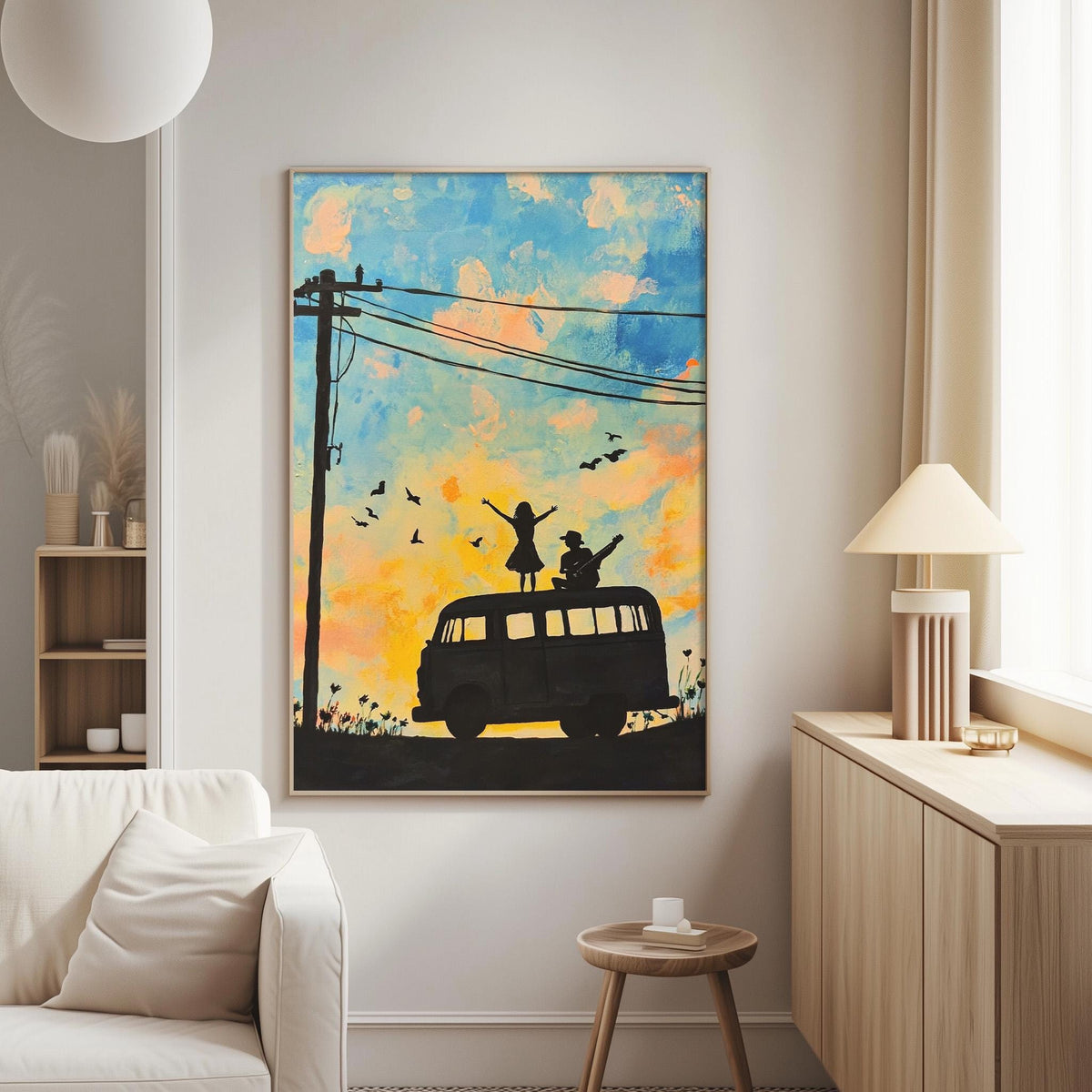 a large painting of a van with silhouettes of people on top, set against a colorful sky with birds. The painting is hung on a wall in a living room, with a white couch and a lamp visible in the background.