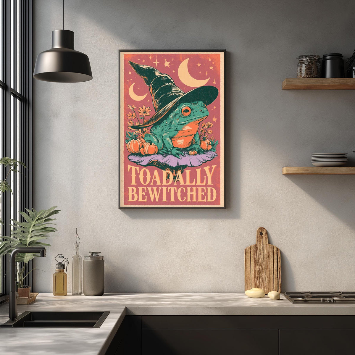 a framed poster of a frog wearing a witch's hat, with the text "Toadally Bewitched" on it, hanging on a wall above a kitchen counter.