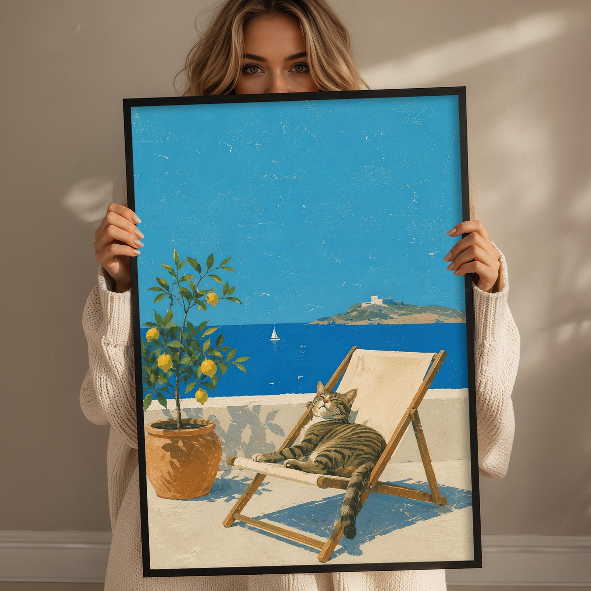 A woman holds up a framed painting depicting a cat lounging in a chair on a balcony overlooking the ocean.