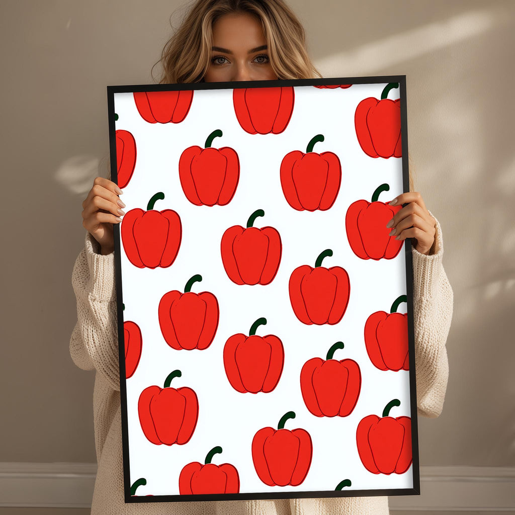 A woman is holding up a framed print with a repeating pattern of red peppers.