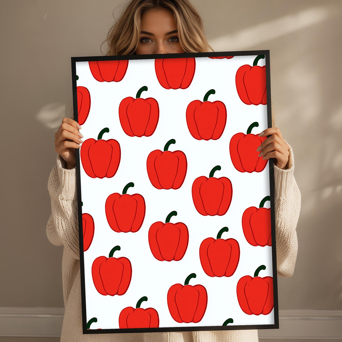A woman is holding up a framed print with a repeating pattern of red peppers.