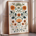 A framed print of a floral design with various flowers and leaves is displayed on a wall in a room with a window.