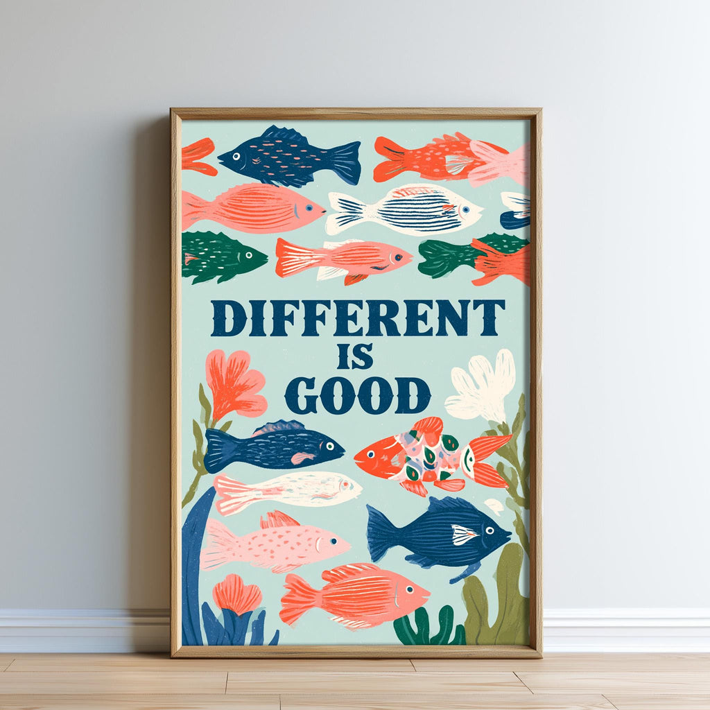 The image is a framed poster with a vibrant illustration of various colorful fish swimming in the ocean. The poster has a motivational message that reads "DIFFERENT IS GOOD" and is displayed on a wall.