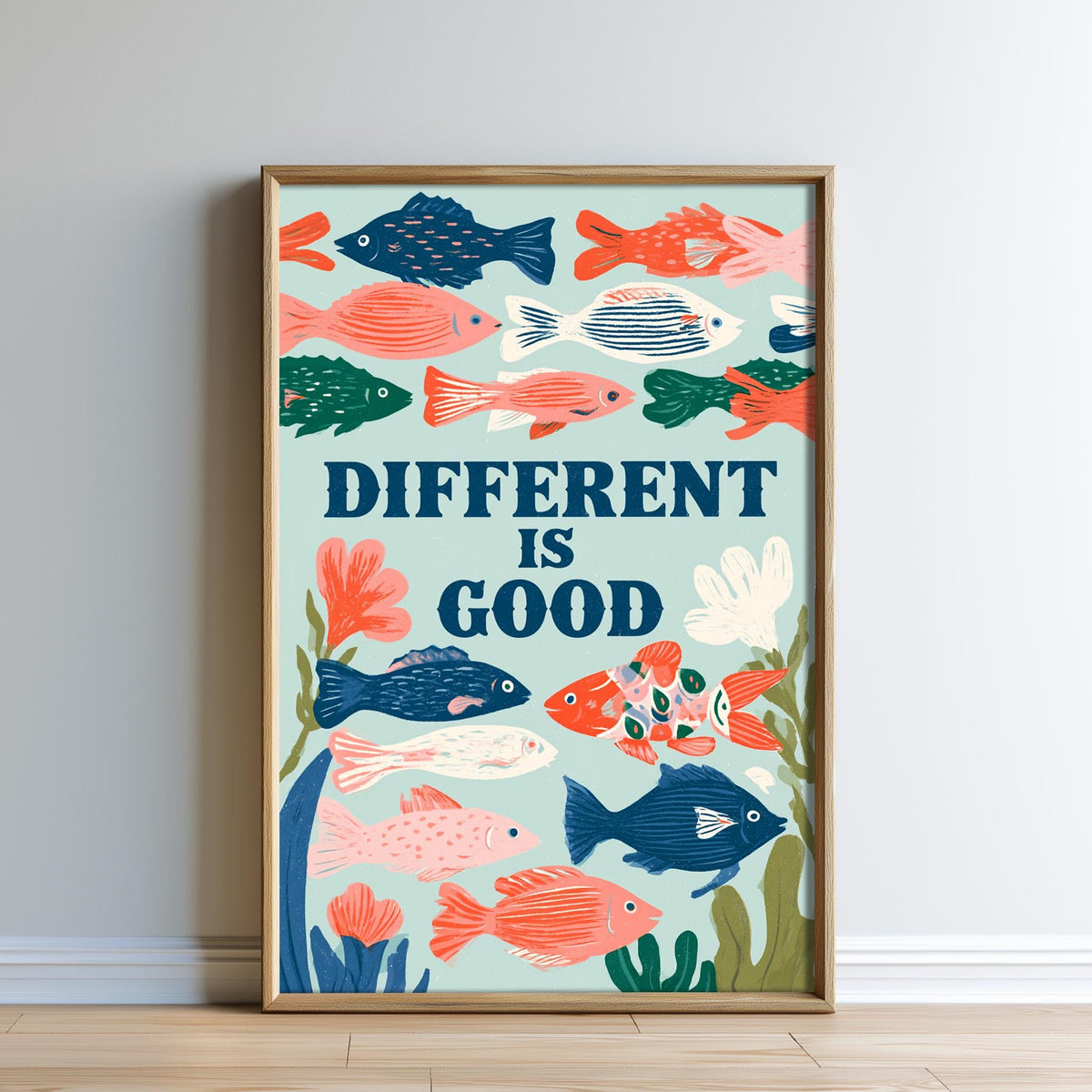 The image is a framed poster with a vibrant illustration of various colorful fish swimming in the ocean. The poster has a motivational message that reads "DIFFERENT IS GOOD" and is displayed on a wall.