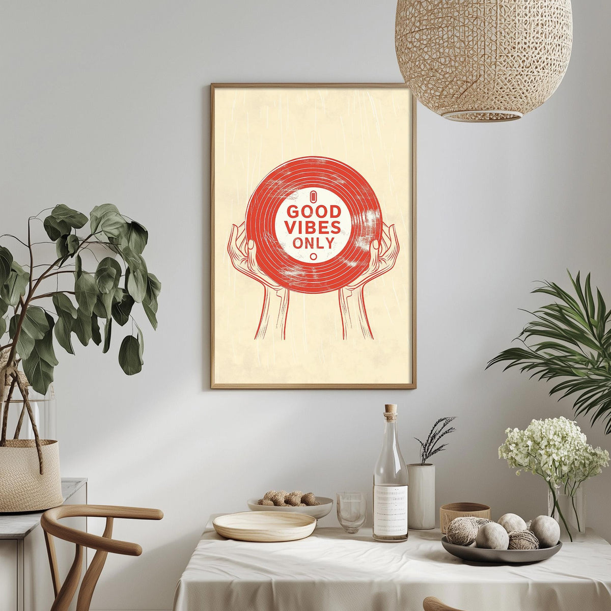a framed poster with the text "GOOD VIBES ONLY" displayed on a wall above a dining table with various items on it, including a bottle, bowls, and a vase.