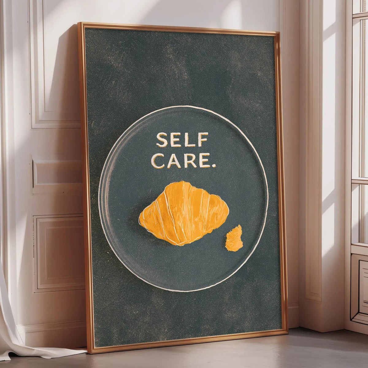 a framed poster with the text "SELF CARE" and an illustration of a croissant on a dark background.