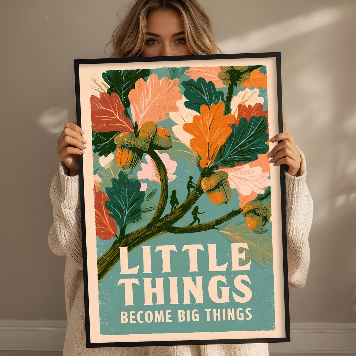 A woman holding a framed poster with a colorful illustration of leaves and flowers, along with the text "LITTLE THINGS BECOME BIG THINGS".