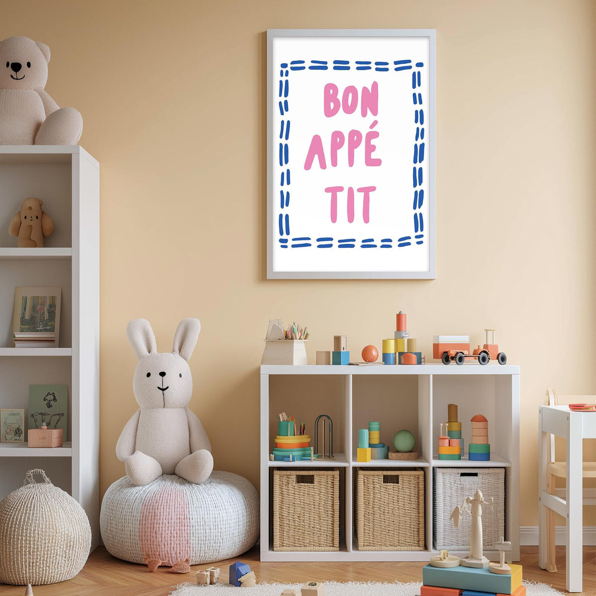 A child's bedroom with a white bookshelf, a stuffed rabbit, and a toy train. Above the bookshelf is a framed poster with the text " bon appé tit" in pink and blue.