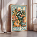 a framed poster with a raccoon holding a piece of fruit, surrounded by autumn-themed elements such as flowers and pumpkins.