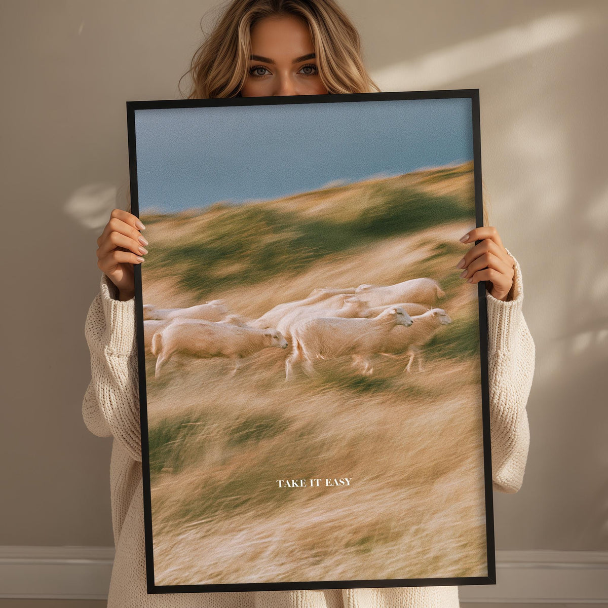 A woman holding a framed picture of a herd of sheep in a field.