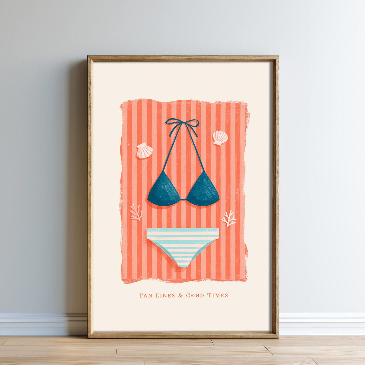A framed illustration of a bikini top and bottoms against a striped background, accompanied by the text "TAN LINES & GOOD TIMES".