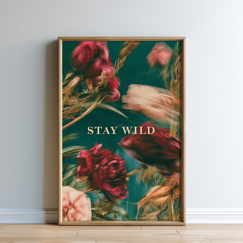 The image is a framed poster with a vibrant floral design featuring red and pink flowers against a teal background. The text "STAY WILD" is prominently displayed in the center of the poster.