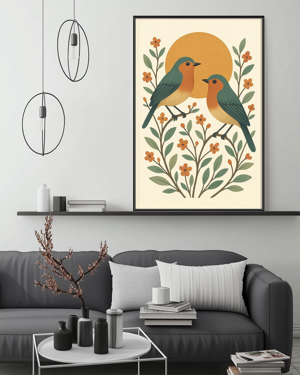 a cozy living room with a gray sofa, a coffee table, and a framed print of two birds perched on branches with flowers and leaves. The room has a minimalist and modern design, with pendant lights hanging above the sofa and a shelf displaying decorative items.