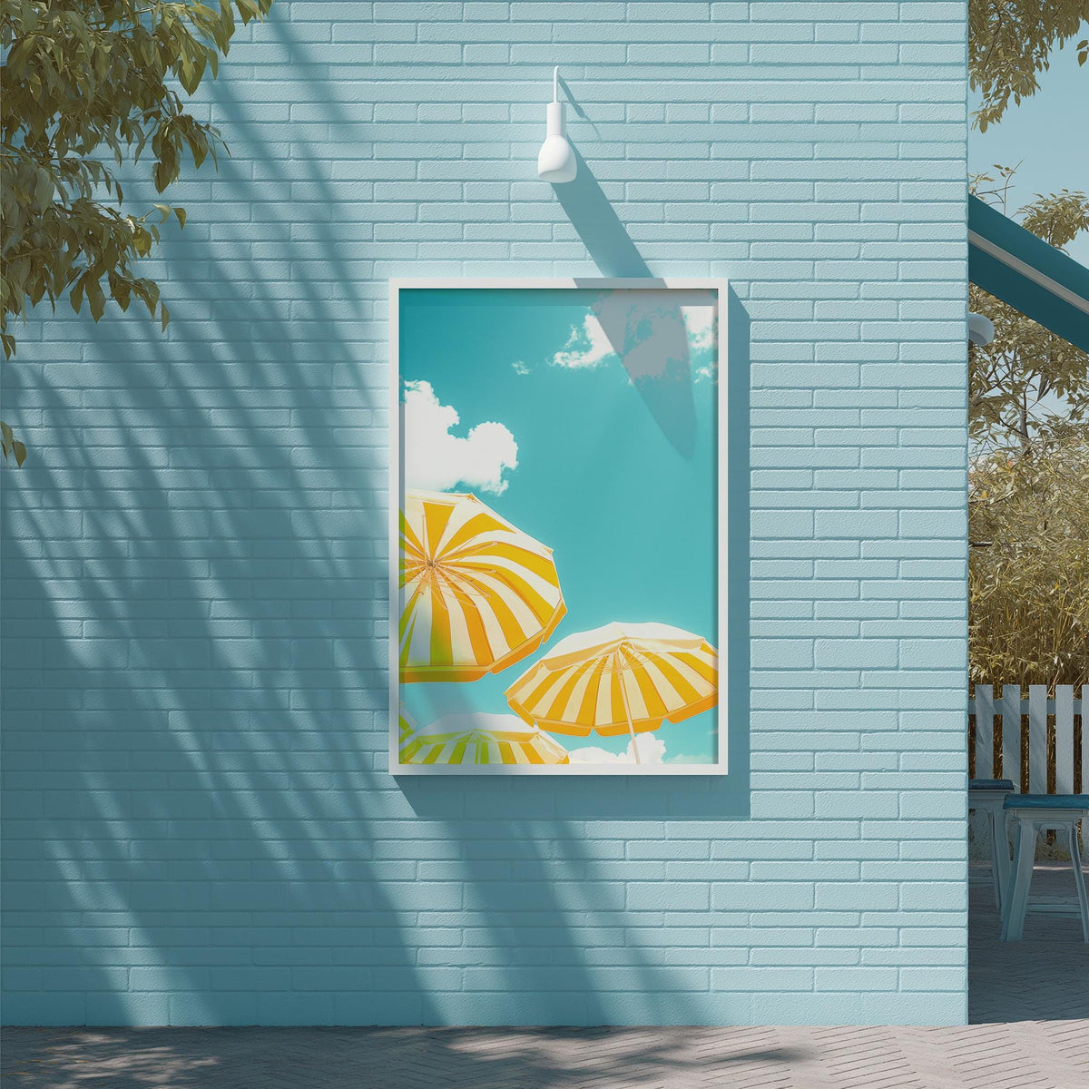 a blue brick wall with a framed picture of three yellow and white striped umbrellas against a blue sky with clouds.