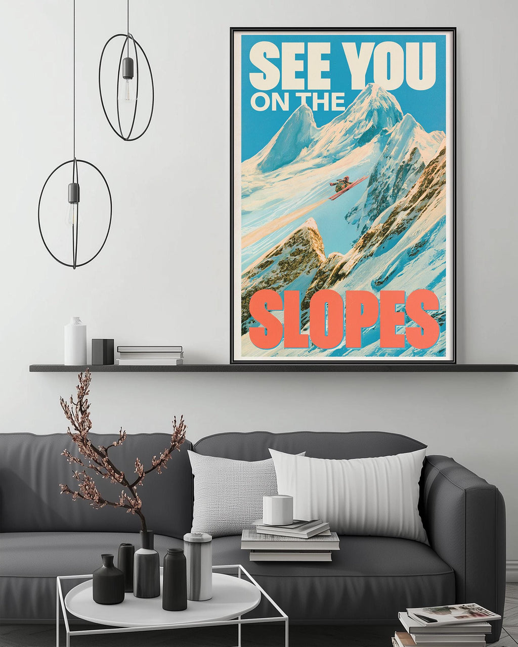 a poster of a mountain slope with a skier, hanging on a wall above a gray couch with a coffee table in front of it.